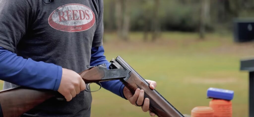 A man holds a shotgun in disassembled condition